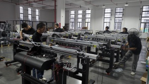 Xinflying technicians assemble and wire multiple DTF printers on a busy factory production floor.