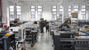 Workers inspect and assemble rows of Xinflying DTF printers in a bright, organized workshop.