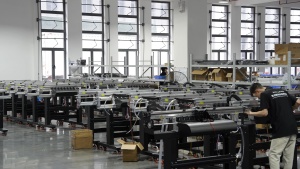 A Xinflying technician works on a DTF printer frame surrounded by machines in different stages of assembly.