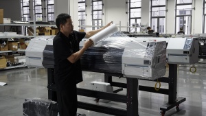 A worker applies protective stretch film to a completed Xinflying DTF printer before storage or shipment.