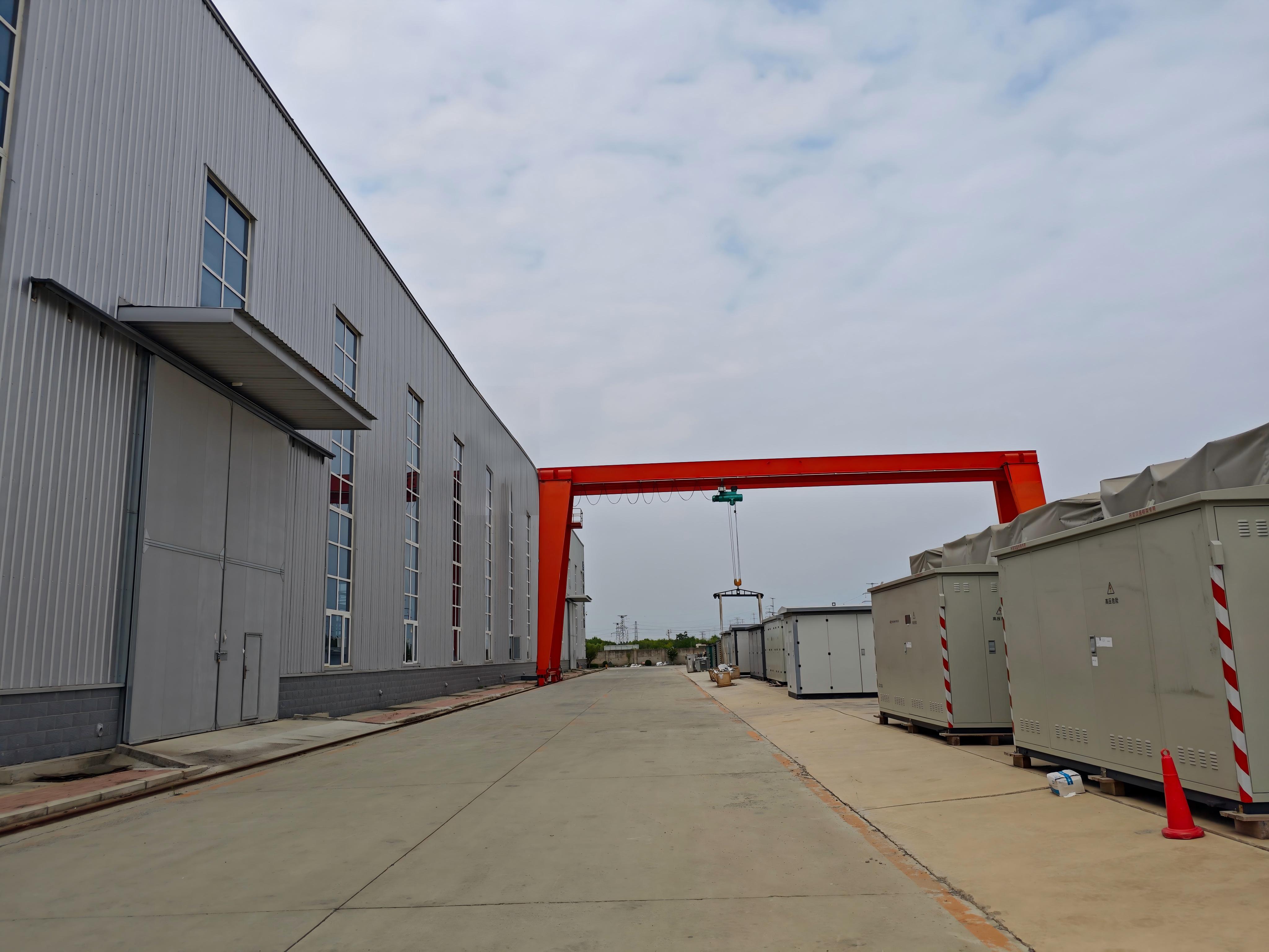 Exterior of Milestone Electrical's transformer factory, including the main production buildings, outdoor gantry crane, and prefabricated substations stored in the factory yard. The outdoor area is used for equipment handling and storage before delivery.