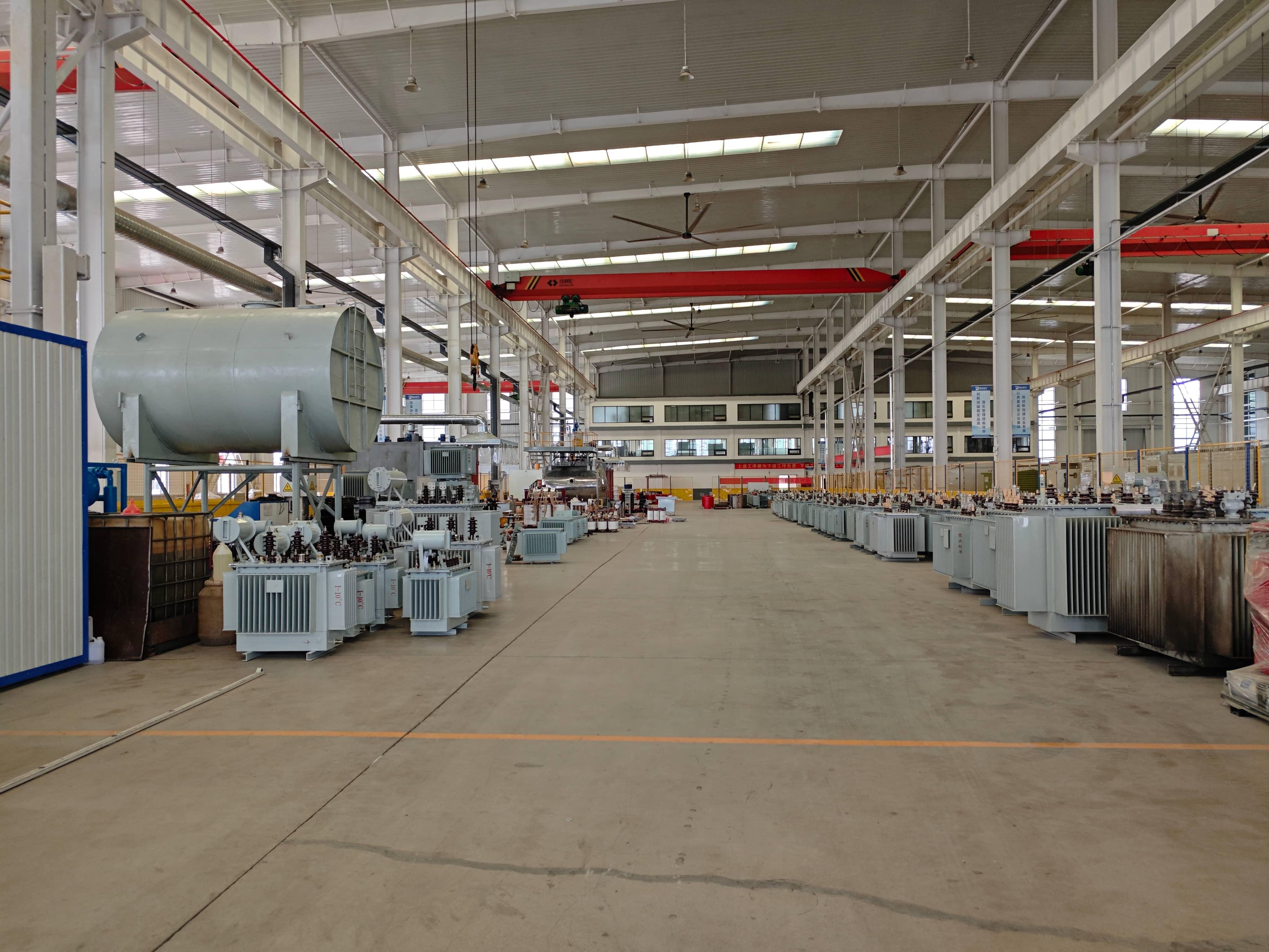 Transformer manufacturing workshop with core assembly stations, vacuum drying equipment, oil filling facilities, and finished transformers. The production area is used for transformer assembly, insulation processing, and preparation of completed units.