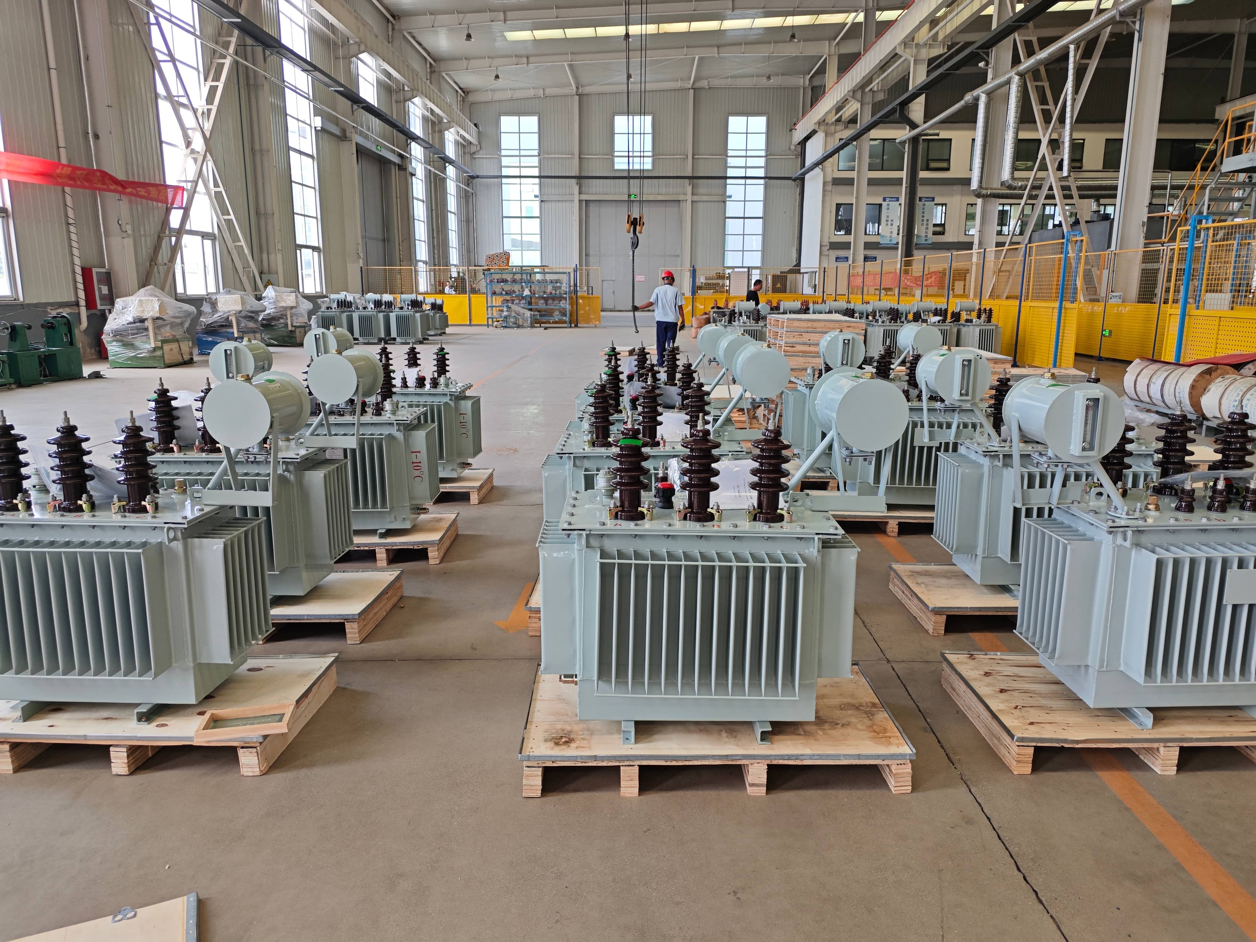 Finished transformer storage and packing area, where workers use overhead lifting equipment to move completed transformers. The transformers are arranged for handling, packing, and preparation for shipment to customers.
