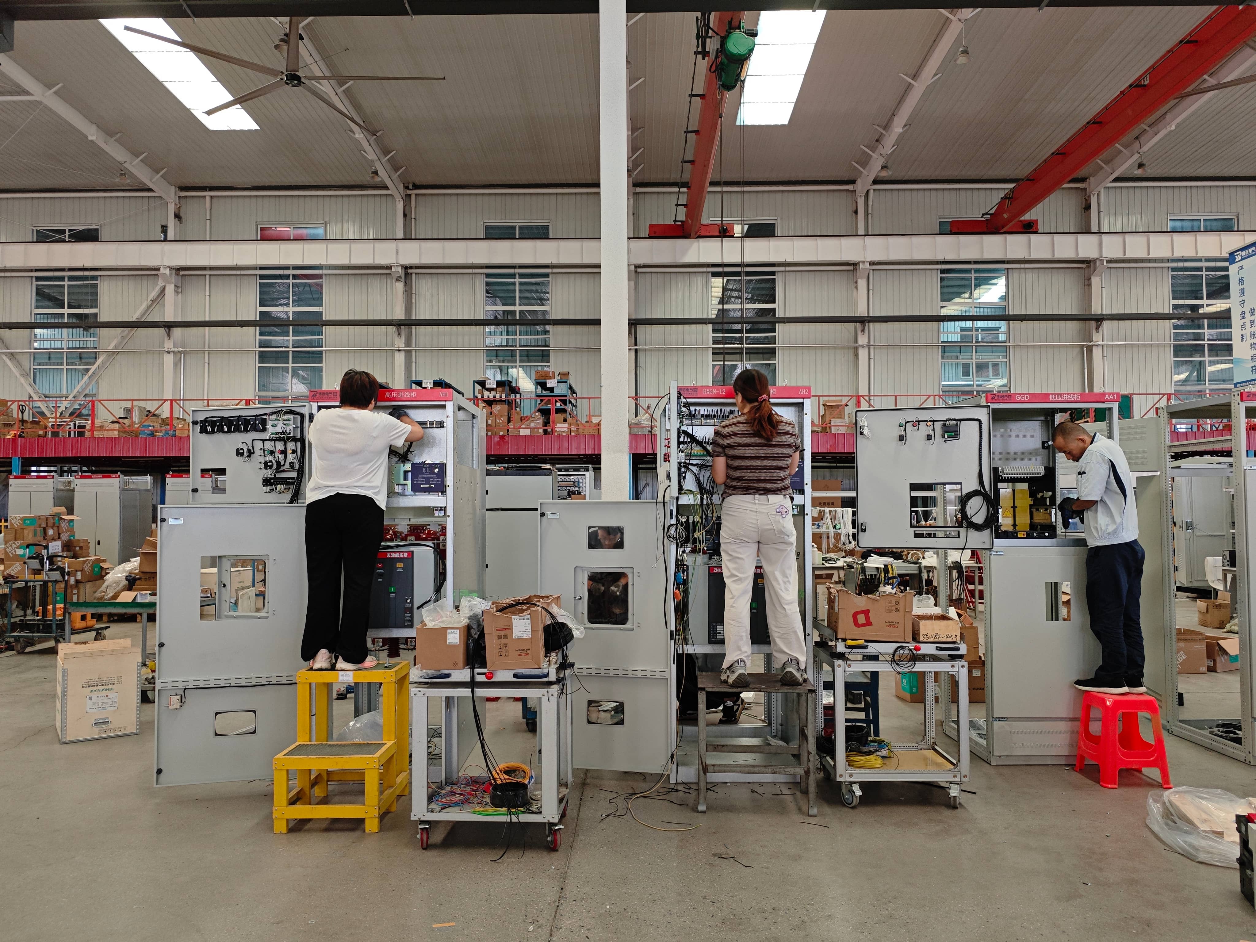 Factory technicians installing electrical components inside a prefabricated substation, including circuit breakers, disconnect switches, instrument transformers, and related equipment. Assembly work includes component mounting, positioning, and electrical connections according to the substation design.