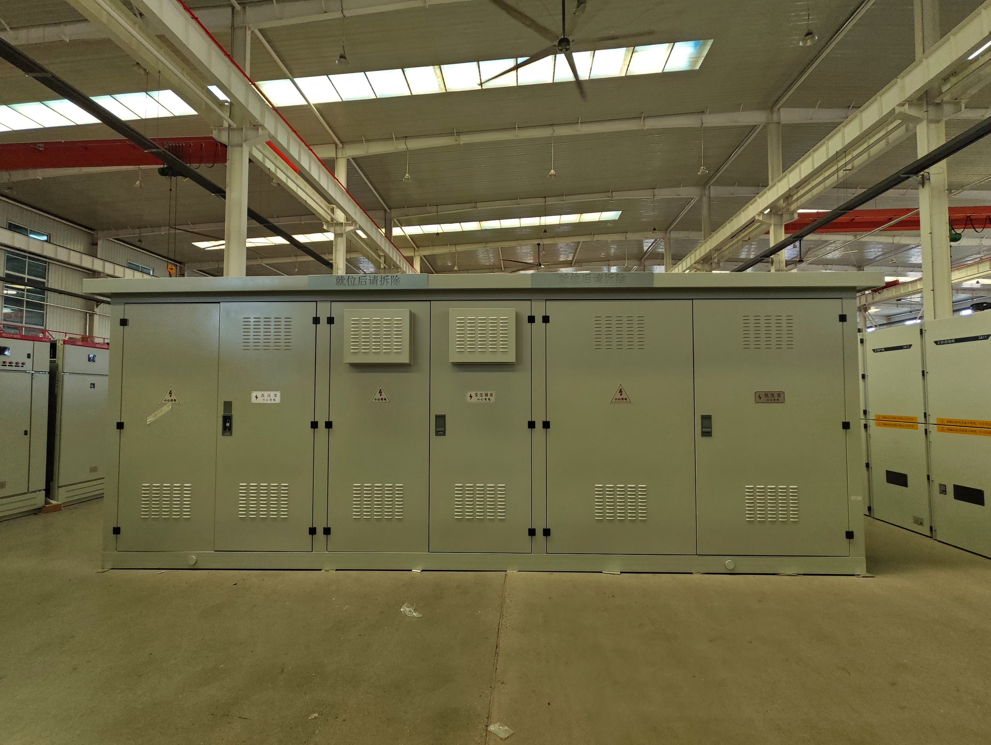 Indoor finished goods warehouse containing assembled compact substations and prefabricated power distribution units. The warehouse provides storage space for completed electrical equipment before packing, loading, and shipment to domestic and international customers, with units organized for order fulfillment and delivery preparation.